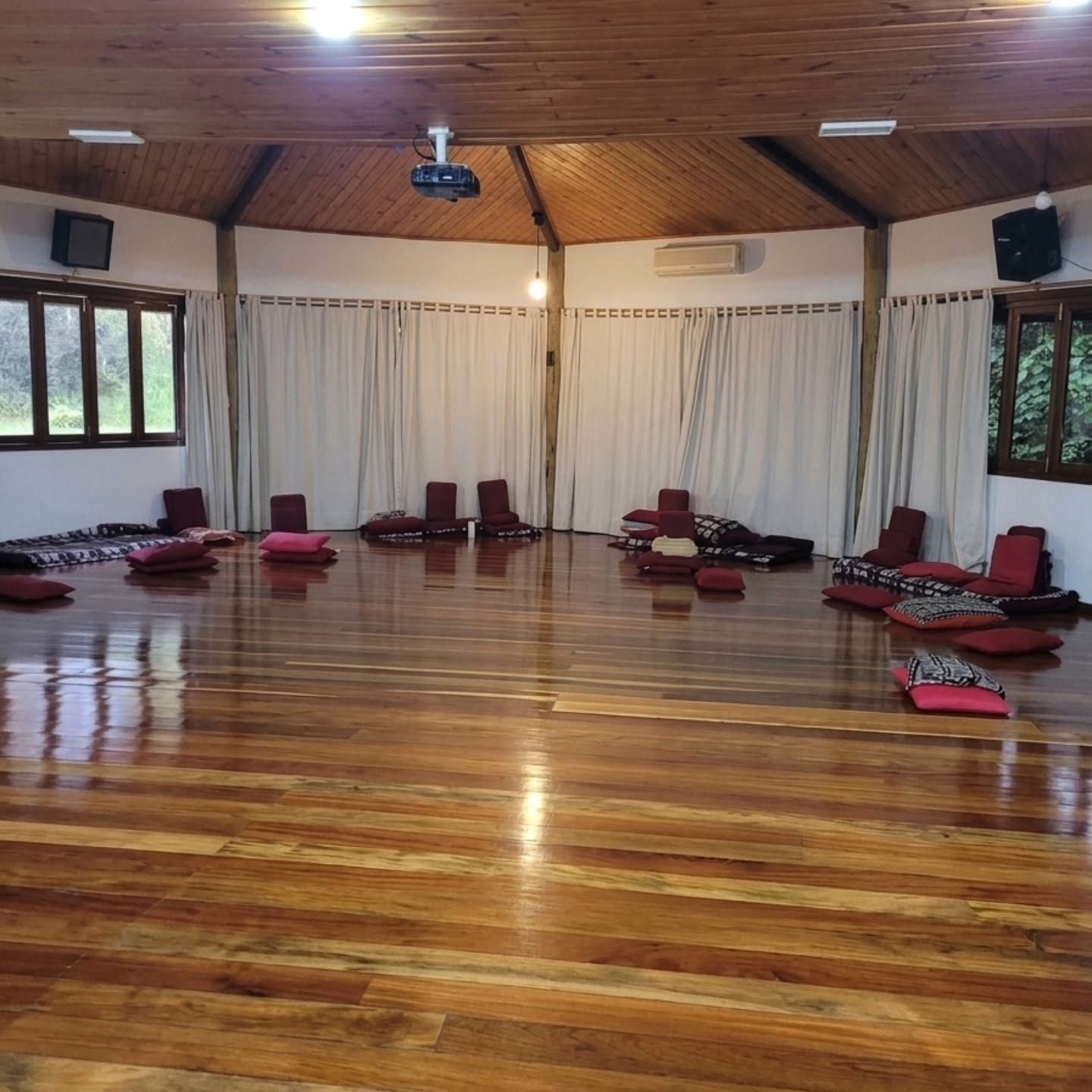 Sala com piso de madeira e almofadas dispostas em roda